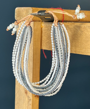 Load image into Gallery viewer, The Shanga Slide Beaded Bracelet by Her Best Foot Forward features layered white and metallic gray beads with a tan cord, inspired by Maasai jewelry from East Africa—an easy slip-on accessory with unique bead accents.