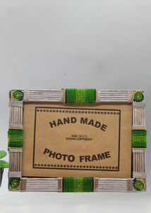 The Picha Handmade Beaded Photo Frame by Her Best Foot Forward features green and silver beads, crafted by East African women, with a “HAND MADE PHOTO FRAME” insert and a plant leaf detail—ideal for sustainable home decor.