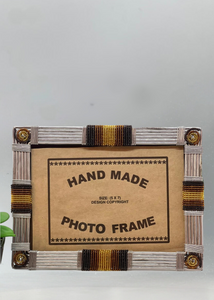 The Picha Handmade Beaded Photo Frame by Her Best Foot Forward features gold, brown, and black beadwork. Crafted by East African women, this 5x7 sustainable decor piece includes a cardboard insert—perfect beside a green plant.