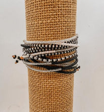Load image into Gallery viewer, The Shanga Slide Beaded Bracelet by Her Best Foot Forward features black, white, and silver Maasai-inspired beads on a brown display, capturing East African artistry against a plain white background.