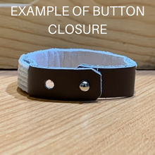 Load image into Gallery viewer, The Share the LOVE Beaded Bracelet by Her Best Foot Forward, inspired by handmade Maasai jewelry from East Africa, features a brown and white leather wristband with button closure. EXAMPLE OF BUTTON CLOSURE appears above it on a wooden surface.