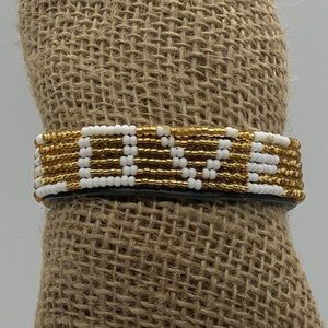 The Share the LOVE Beaded Bracelet by Her Best Foot Forward features white beads spelling LOVE among gold beads—a meaningful, handmade Maasai jewelry piece from East Africa, perfect as a unique and thoughtful gift.