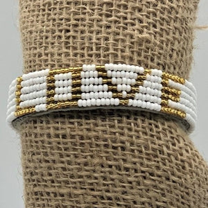 The Share the LOVE Beaded Bracelet by Her Best Foot Forward is handmade in East Africa, inspired by Maasai jewelry, with gold and white beads spelling LOVE—a beautiful, meaningful gift.