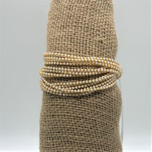 Load image into Gallery viewer, The Shanga Slide Beaded Bracelet by Her Best Foot Forward features alternating white and gold beads, inspired by Maasai jewelry. This handcrafted bracelet from East Africa is displayed on a textured burlap stand against a plain background.