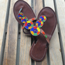 Load image into Gallery viewer, A pair of Kelly Handmade Beaded Sandals from Her Best Foot Forward, crafted with Maasai beadwork in vibrant colors, displayed on wood—sophisticated ethical footwear perfect for summer.