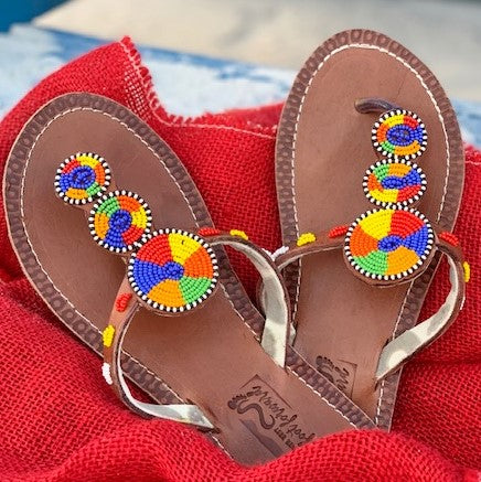 The Kelly Handmade Beaded Sandals by Her Best Foot Forward feature brown leather and vibrant Maasai beadwork in red, yellow, green, blue, and orange—an artisanal, ethical choice for summer style.