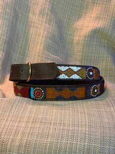 The Savanna Beaded Dog Collar by Her Best Foot Forward features vibrant Maasai beadwork—diamond and circular patterns in red, blue, white, orange, and yellow—handmade in East Africa and shown on a textured beige background.