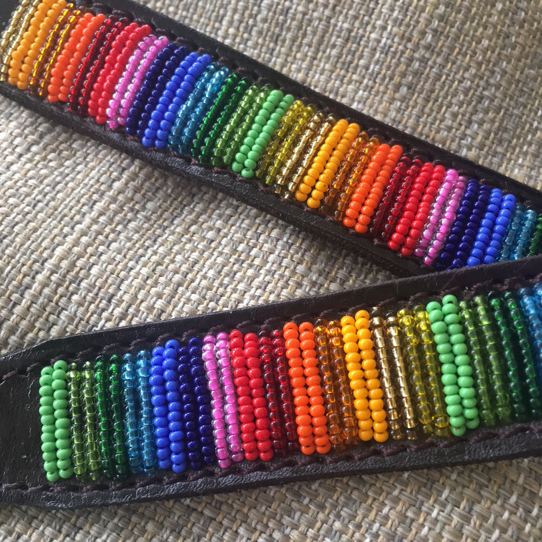 Two black straps with colorful Maasai beads rest on textured beige fabric, highlighting the vibrant Her Best Foot Forward Ethan Almighty Beaded Dog Collar—an ethical, handmade pet accessory from East Africa.