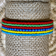 Load image into Gallery viewer, Five vibrant Safari Stripes Beaded Bracelets by Her Best Foot Forward—handmade Maasai jewelry with alternating stripes—add striking East African charm to your style, displayed on woven beige fabric.