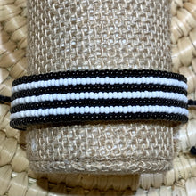 Load image into Gallery viewer, The Safari Stripes Beaded Bracelet by Her Best Foot Forward is a handmade Maasai-inspired accessory from East Africa, featuring alternating black and white beaded stripes, beautifully presented on a woven beige surface.