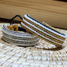Load image into Gallery viewer, The Safari Stripes Beaded Bracelet by Her Best Foot Forward is a handmade Maasai-inspired piece from East Africa, featuring alternating stripes of small white beads with gold and silver accents, beautifully presented on a woven surface.