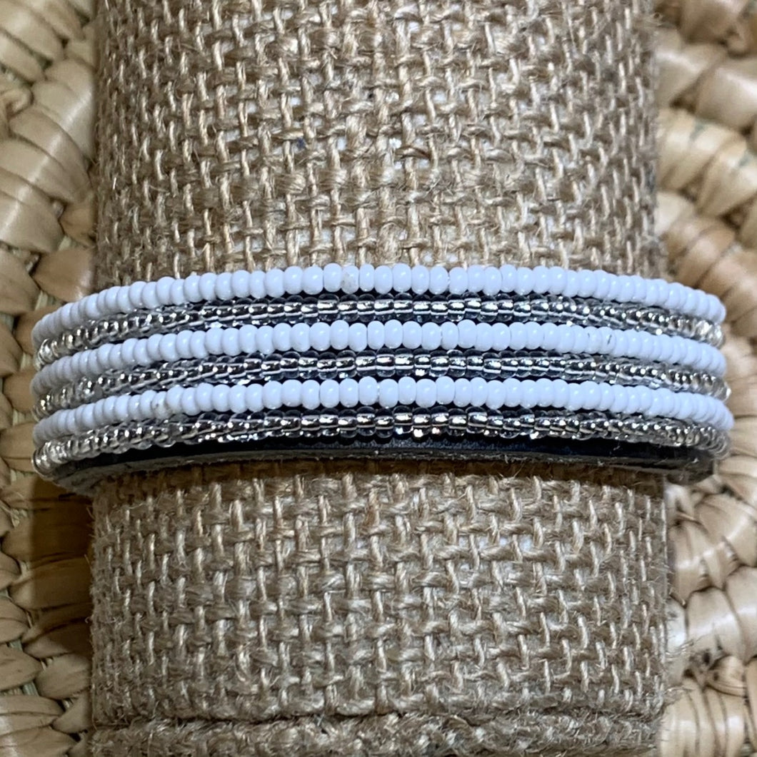 A close-up of the Safari Stripes Beaded Bracelet by Her Best Foot Forward, handmade Maasai jewelry from East Africa, displayed on a beige stand with a woven straw background.