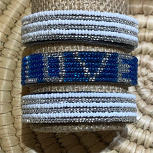 Load image into Gallery viewer, The Safari Stripes Beaded Bracelet by Her Best Foot Forward is displayed on a textured stand. This handmade Maasai jewelry from East Africa features alternating stripes and stands out against a woven, straw-like background.