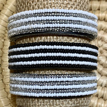 Load image into Gallery viewer, The Safari Stripes Beaded Bracelet by Her Best Foot Forward is handmade Maasai jewelry from East Africa featuring alternating stripes of white, black, and silver beads, beautifully displayed on a woven surface.