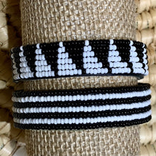 Load image into Gallery viewer, Her Best Foot Forwards Safari Stripes Beaded Bracelet—handmade Maasai jewelry from East Africa—rests on a textured beige surface, showcasing its distinctive alternating black and white stripes.
