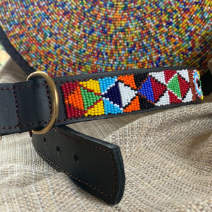 The Tapestry Beaded Dog Collar by Her Best Foot Forward showcases intricate, handmade Maasai patterns and a brass buckle, crafted ethically in East Africa—an eye-catching pet accessory resting on woven fabric.