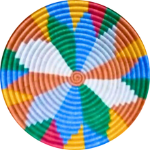 Load image into Gallery viewer, The Sunrise Handwoven Basket Lid by Her Best Foot Forward features a vibrant spiral design in blue, green, orange, yellow, white, and red—perfect as geometric wall or table decor. Crafted from sweet grass in East Africa.