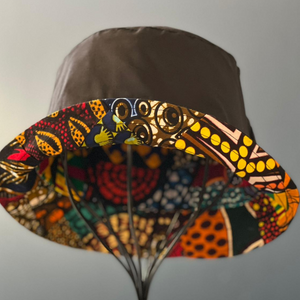 The Ndoo Reversible Bucket Hat by Her Best Foot Forward features traditional East African Kitenge fabric with a vibrant geometric brim in red, yellow, orange, and black, beautifully displayed against a plain background.