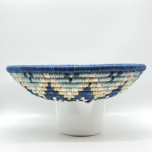 Load image into Gallery viewer, The Sunrise Handwoven Basket by Her Best Foot Forward features a geometric blue, cream, and white design. Crafted from sweet grass in East Africa, its perfect as wall or table decor and looks stunning displayed on a plain white background.