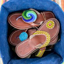 Load image into Gallery viewer, A pair of Her Best Foot Forward Ocean Wave Handmade Beaded Sandals, featuring colorful Maasai beadwork, are placed in a blue fabric basket.