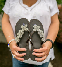 Load image into Gallery viewer, A person in a white shirt and jeans holds the Addison Handmade Beaded Sandals by Her Best Foot Forward, featuring ethical summer footwear with intricate Maasai beadwork.