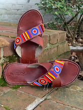 Load image into Gallery viewer, The Jane Handmade Beaded Sandals by Her Best Foot Forward, featuring colorful Maasai beadwork, rest on outdoor brick steps near green bushes and fallen leaves.