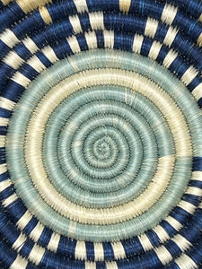 Close-up of the Sunrise Handwoven Basket by Her Best Foot Forward, crafted from sweet grass in East Africa. Blue, cream, and white concentric circles create a textured spiral—ideal as wall decor or a centerpiece.