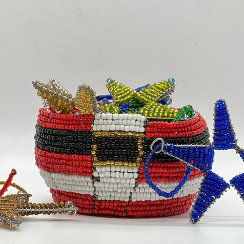 The Santa Baskets by Her Best Foot Forward are handcrafted Christmas baskets from Tanzania, featuring a colorful Santa belt design and holding beaded star ornaments in blue, gold, green, and silver against a plain white background.