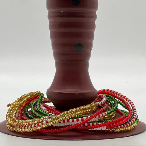 The SHANGA 14-Strand Beaded Bracelet by Her Best Foot Forward, a handmade Maasai jewelry piece in holiday colors, is wrapped around the base of a brown cylindrical object against a plain white background.
