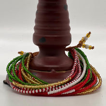 Load image into Gallery viewer, Her Best Foot Forward’s Shanga Slide Beaded Bracelet—an easy slip-on Maasai jewelry piece from East Africa—features vibrant red, green, white, and gold beads displayed around a brown, spotted cylinder on a plain white background.