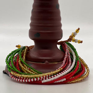 Her Best Foot Forward’s Shanga Slide Beaded Bracelet—an easy slip-on Maasai jewelry piece from East Africa—features vibrant red, green, white, and gold beads displayed around a brown, spotted cylinder on a plain white background.
