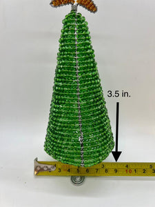 The 3.5 Hand-Beaded Christmas Tree by Her Best Foot Forward is handcrafted in Tanzania from reclaimed wire, featuring festive decorations and topped with a gold ornament. A measuring tape highlights its small, conical shape.