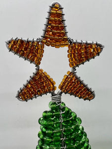 A star-shaped tree topper of orange beads and wire crowns the Hand-Beaded Christmas Trees by Her Best Foot Forward, highlighting Tanzanian women artisans’ craftsmanship with reclaimed wire against a plain, light background.