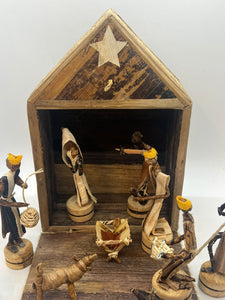 The Handmade Nativity Set by Her Best Foot Forward is a fair wage Christmas decor from Tanzania, featuring Mary, Joseph, baby Jesus in a manger, three wise men with gifts, an angel, and a donkey inside a rustic stable with star.