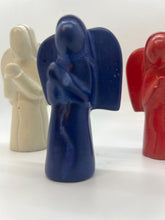 Load image into Gallery viewer, Three Hand-Carved Soapstone Angels by Her Best Foot Forward—white, blue, and red—stand in a row on a white background, with focus on the blue Divine Decor from East Africa and the others softly blurred behind.