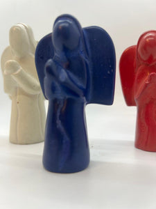 Three Hand-Carved Soapstone Angels by Her Best Foot Forward—white, blue, and red—stand in a row on a white background, with focus on the blue Divine Decor from East Africa and the others softly blurred behind.