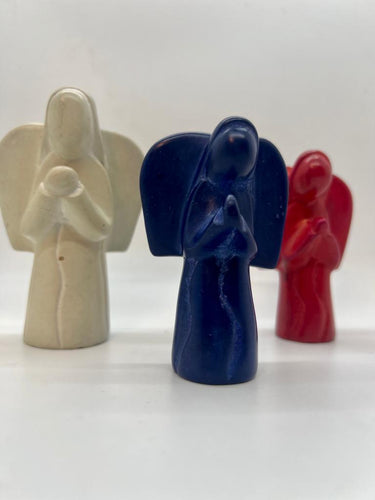 Three small Hand-Carved Soapstone Angels by Her Best Foot Forward—one white, one dark blue, and one red—stand upright on a white surface. The blue angel is in front, ideal for Christmas home decor. Divine Decor from East Africa.