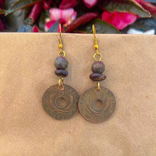 Load image into Gallery viewer, Pesa Currency Coin Earrings by Her Best Foot Forward—handmade from East African coins with central holes, round beads, and gold hooks. Shown on a tan background with blurred pink and green foliage—a unique handmade jewelry gift.