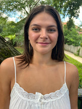 Load image into Gallery viewer, A young woman with straight brown hair and a white tank top smiles outdoors, wearing Shaba Brass Beaded Earrings by Her Best Foot Forward—handmade statement jewelry from East Africa—standing in front of greenery on a sunny day.