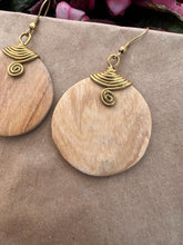 Load image into Gallery viewer, Close-up of Her Best Foot Forward’s Rosemiti Hand-Carved Rosewood Earring, a round statement piece with brass accents, set against a beige background with pink flowers in the upper corner.