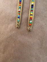 Load image into Gallery viewer, The Shaba Brass Beaded Earrings by Her Best Foot Forward feature vertical rows of vibrant beads, handmade in East Africa. These bold statement earrings bring colorful style to any look. Photographed on a plain brown textured background.