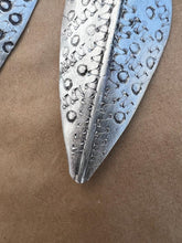 Load image into Gallery viewer, A close-up of the Chuma Etched Metal Earrings by Her Best Foot Forward, featuring textured metal with circular and linear engravings, a raised central vein, and handmade statement style from East Africa.