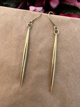 Load image into Gallery viewer, The Shaba Brass Beaded Earrings by Her Best Foot Forward are handmade, long, slender statement jewelry from East Africa, shown on a brown surface with pink and green flowers in the background.