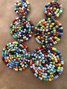 Close-up of Her Best Foot Forward’s Kiungo Conjoined Circle Earrings—handmade Maasai statement jewelry from East Africa—featuring three vibrant, multicolored beaded circles per earring on a brown textured surface.