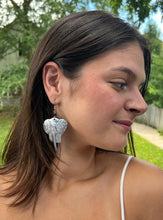 Load image into Gallery viewer, A woman with straight brown hair wears Her Best Foot Forward’s Chuma Etched Metal Earrings—lightweight, handmade statement jewelry from East Africa—while outdoors, looking aside and smiling, greenery softly blurred behind her.