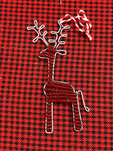 The Reindeer Friends ornament by Her Best Foot Forward is a handcrafted, beaded holiday decoration from Tanzania featuring detailed antlers and a hanging loop, displayed on red and black checkered fabric.