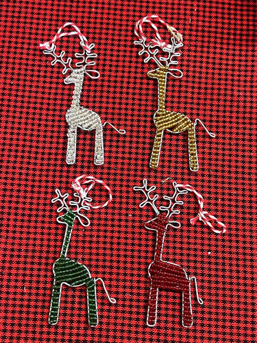 Her Best Foot Forwards Reindeer Friends are handcrafted beaded ornaments from Tanzania. Each festive reindeer in white, gold, green, and red with white antlers and a red & white loop is displayed on a checkered fabric background.