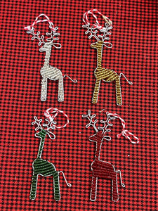 Her Best Foot Forwards Reindeer Friends are handcrafted beaded ornaments from Tanzania. Each festive reindeer in white, gold, green, and red with white antlers and a red & white loop is displayed on a checkered fabric background.