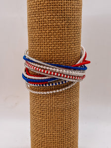 The Shanga Slide Beaded Bracelet by Her Best Foot Forward features easy slip-on Maasai-inspired red, white, blue, and silver beads stylishly wrapped on a display stand.