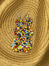 Load image into Gallery viewer, Kiungo Conjoined Circle Earrings by Her Best Foot Forward—handmade Maasai statement jewelry with vibrant circular beadwork—are displayed on woven straw, perfect for fans of bold, artisanal East African accessories.